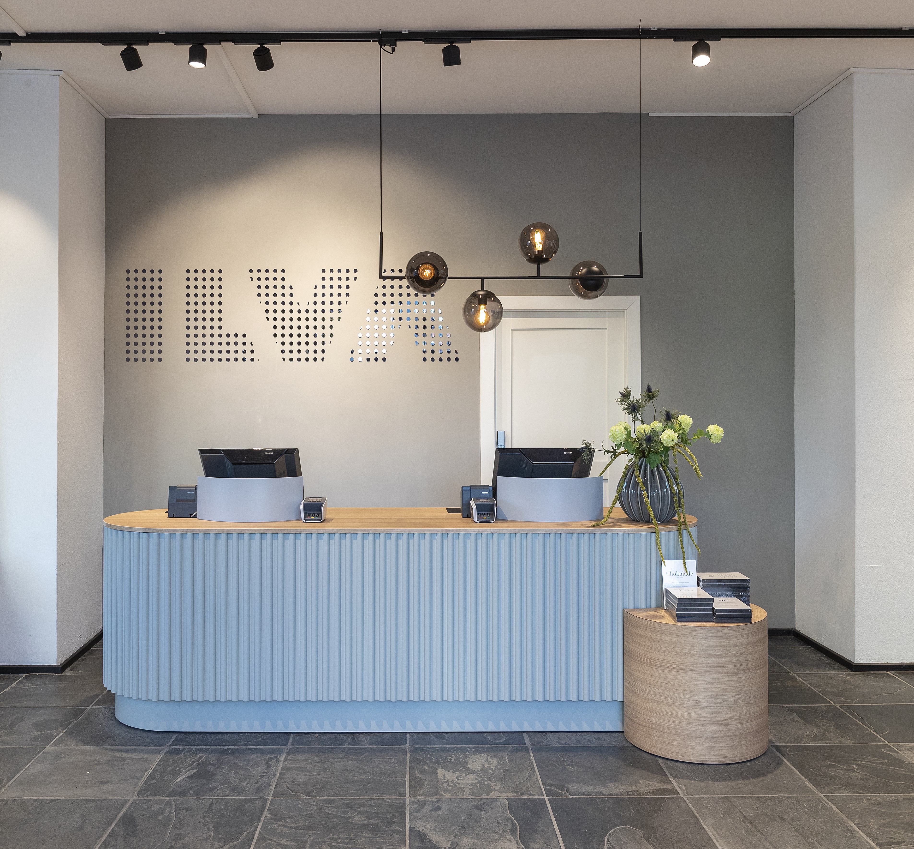 ILVAs eleganta butiksmiljö med en blå och träfärgad kassadisk, moderna pendellampor och en vägg med ILVA-logotypen
