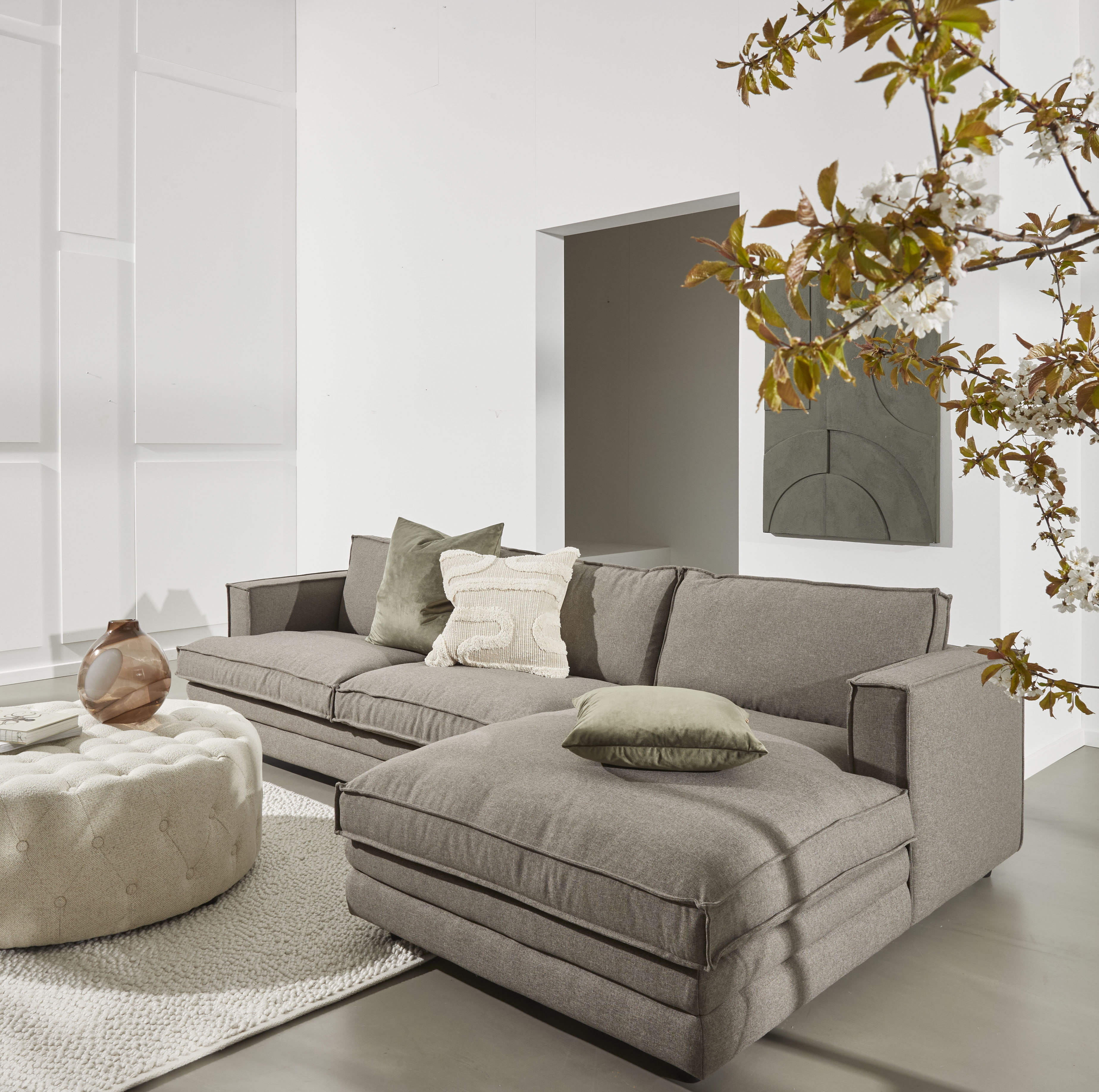 Vardagsrum med stor soffa, kuddar och blomgren