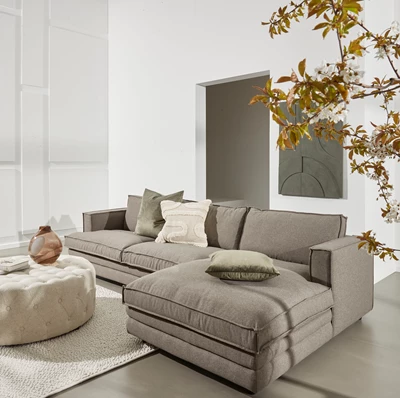 Vardagsrum med stor soffa, kuddar och blomgren