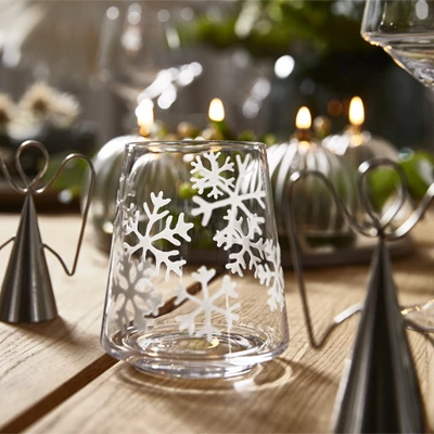 Glas med snöflinga och tänt värmeljus på bordet.