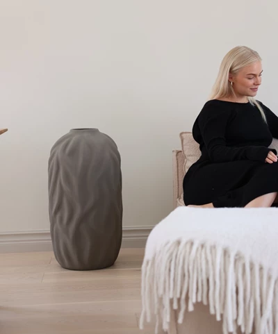 Kvinna sitter avslappnat i stol med grå överkast
