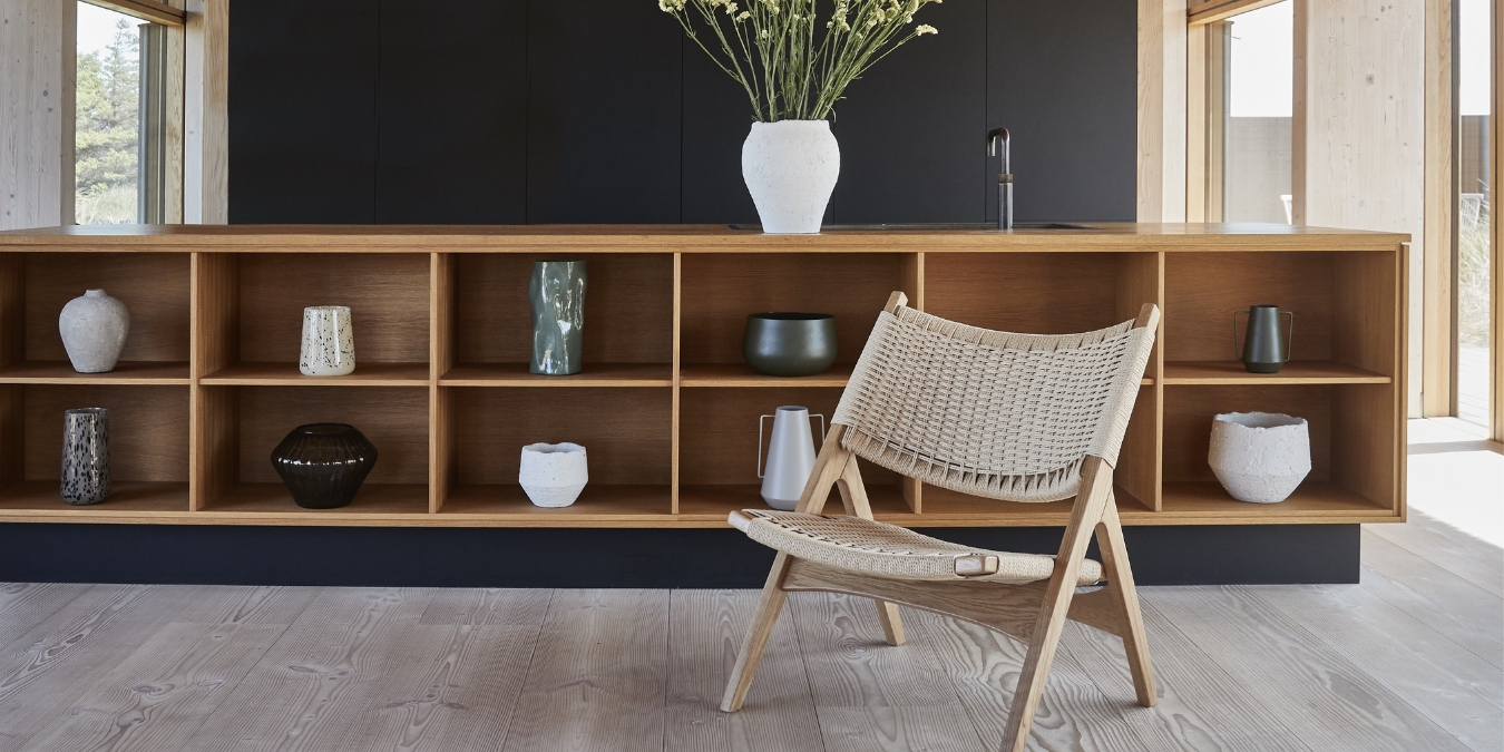 Låg hylla med keramik och flätad stol i trä