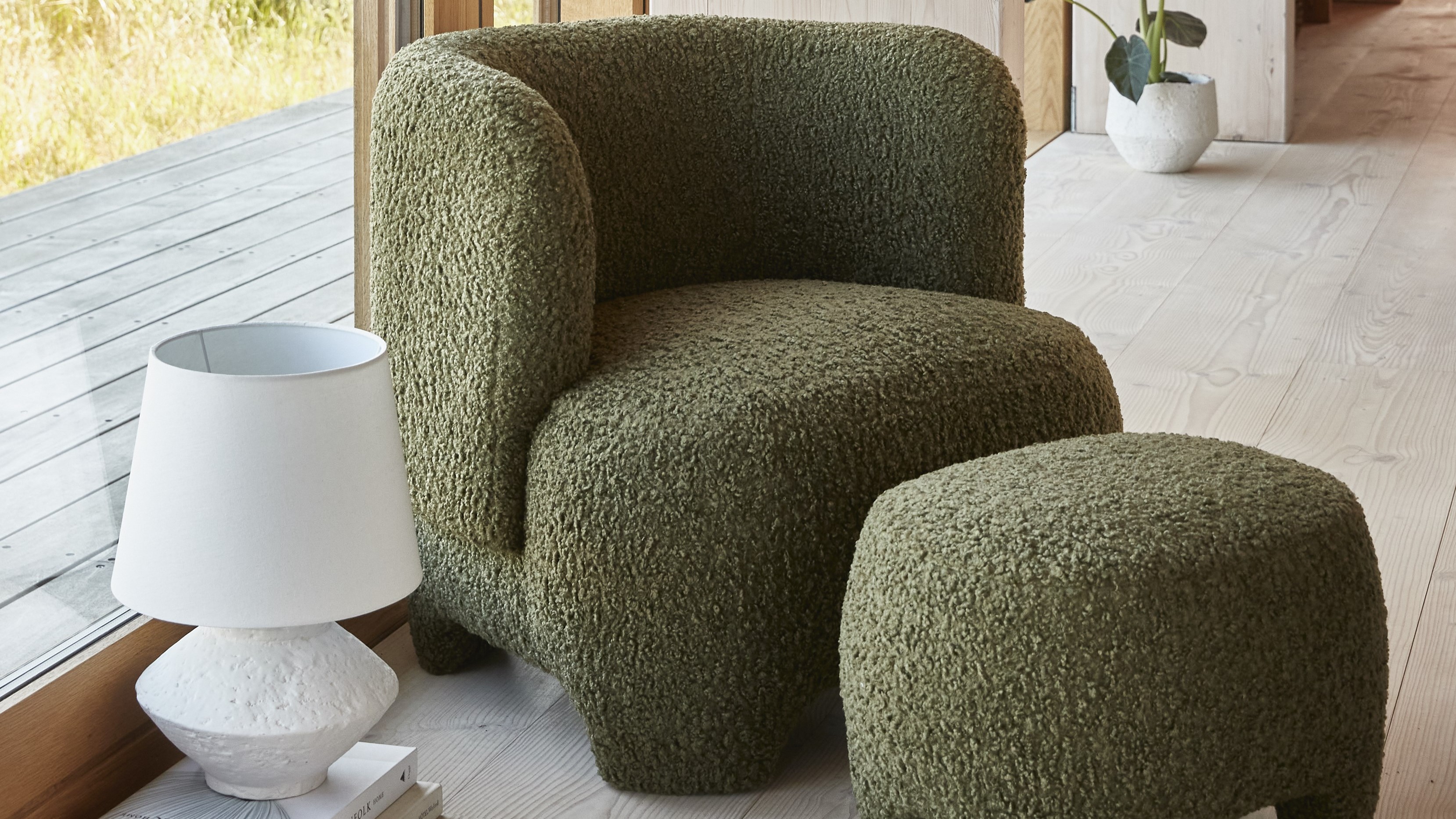 Grön fåtölj med fotpall bredvid vit bordslampa