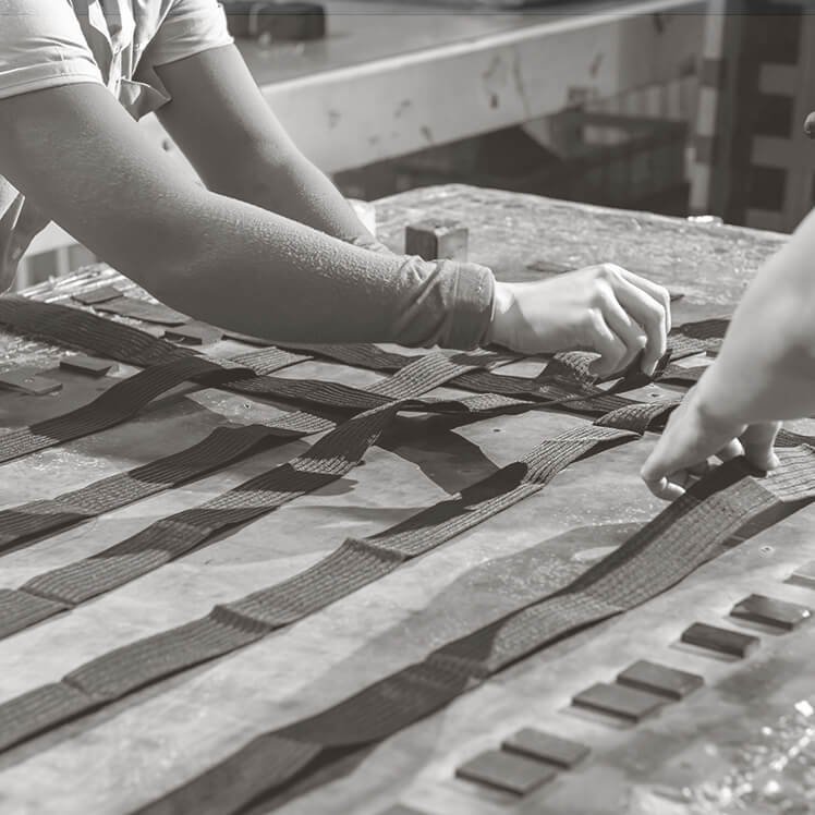 Händer väver band i ett mönster på ett arbetsbord