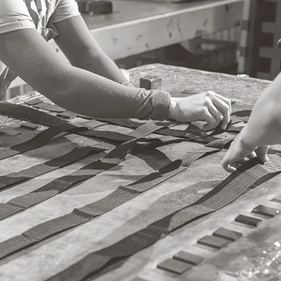 Händer väver band i ett mönster på ett arbetsbord