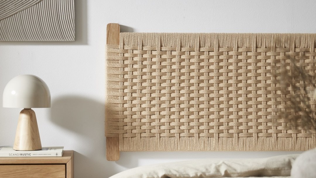 Flätad sänggavel i naturfärgat material på vägg