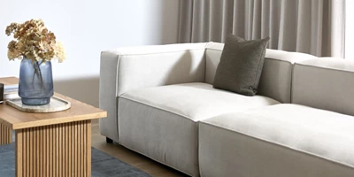 Vit modulsoffa med ett soffbord i trä framför. På bordet står en blå vas med torkade blommor.