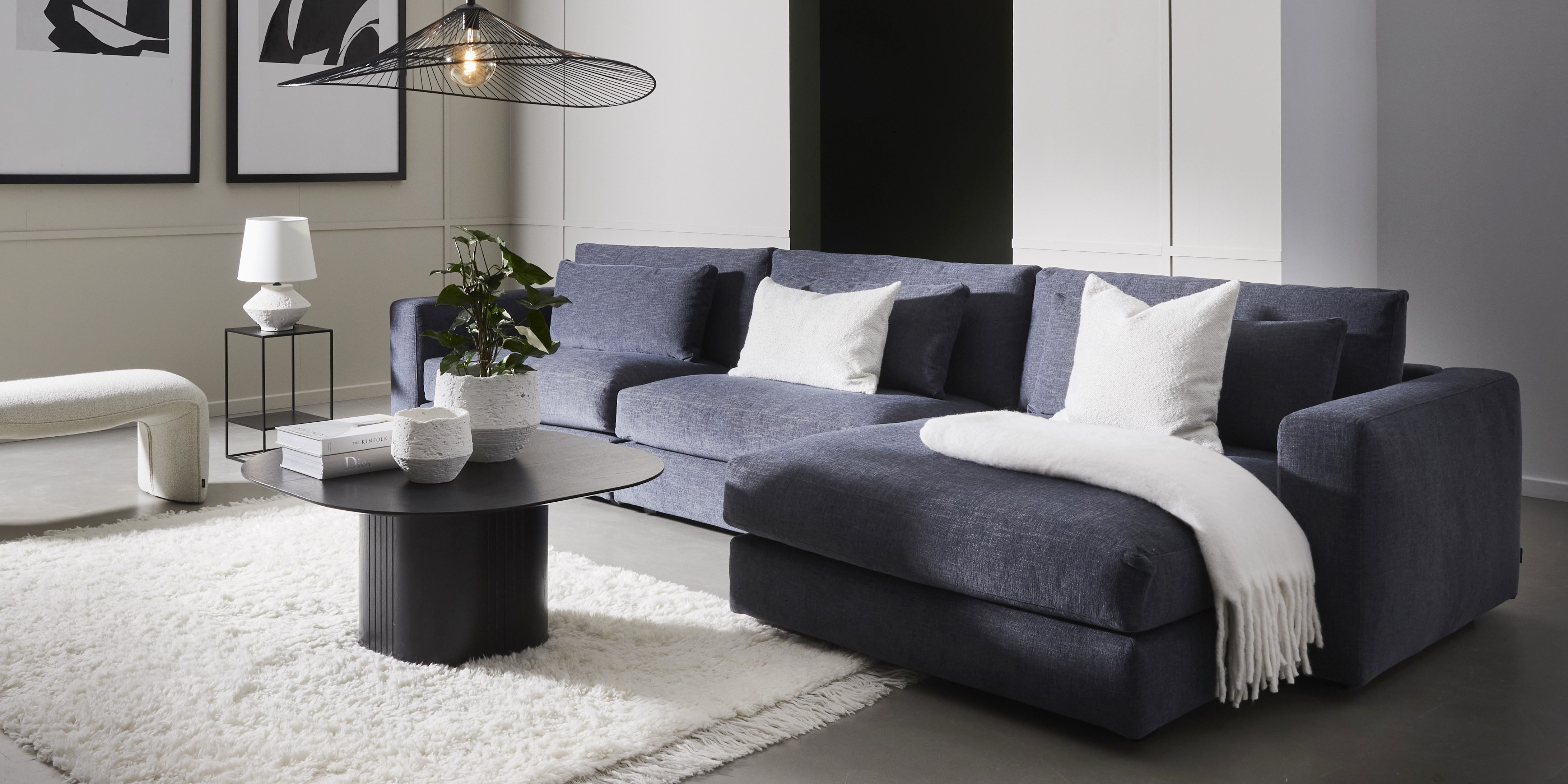 Blå modulsoffa med schäslong. På soffan ligger en vit pläd.