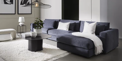 Blå modulsoffa med schäslong. På soffan ligger en vit pläd.