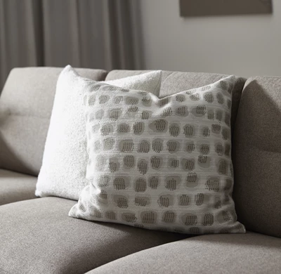 Två prydnadskuddar på soffa. Den ena är vit och den andra är prickig.