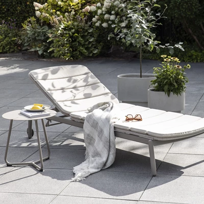 En bild av en vit solstol vid en pool med en filt, en bok och solglasögon på stolen. Bredvid stolen står ett bord med snacks och en kopp.