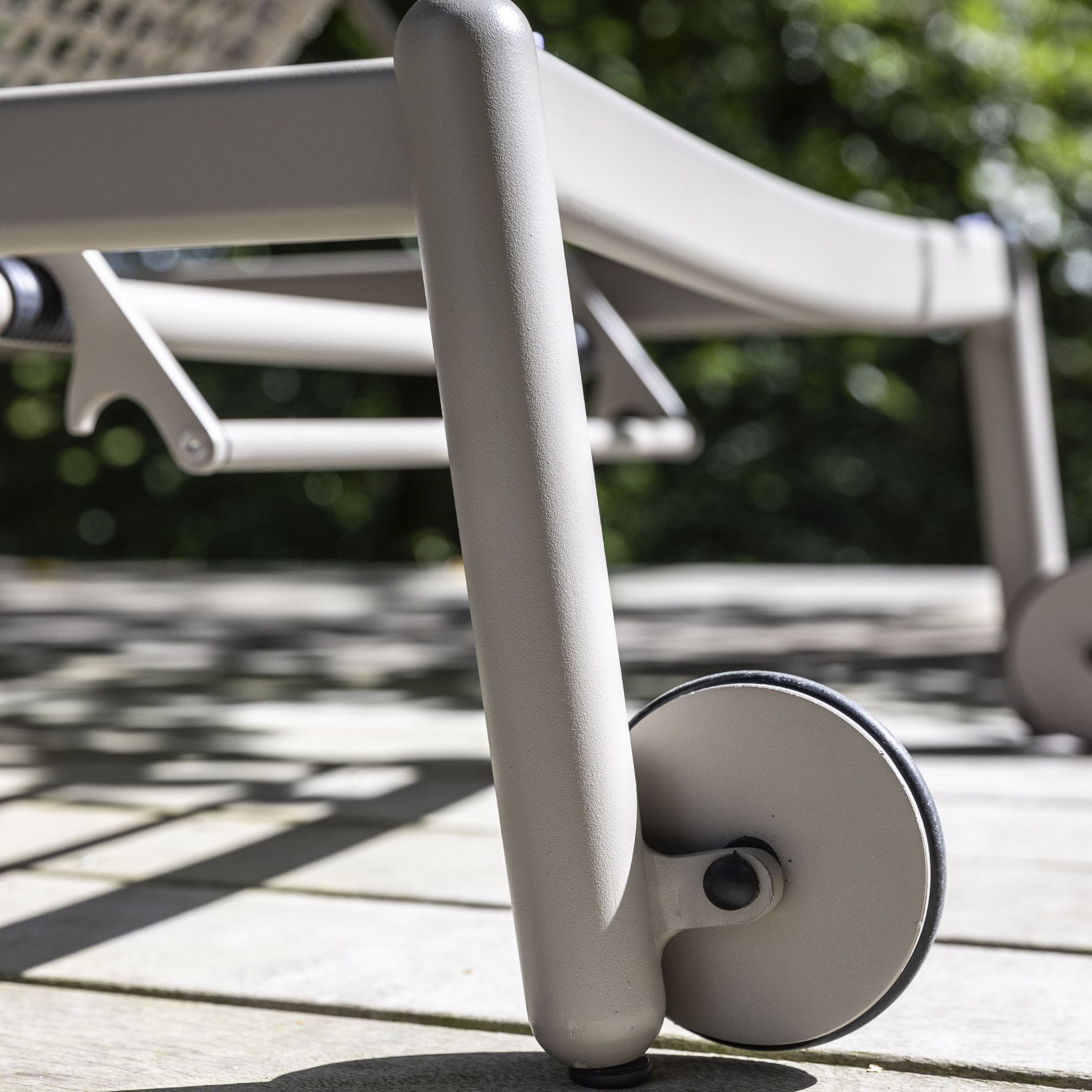 Närbild av ben och hjul på en modern solstol på en terrass med skuggiga mönster