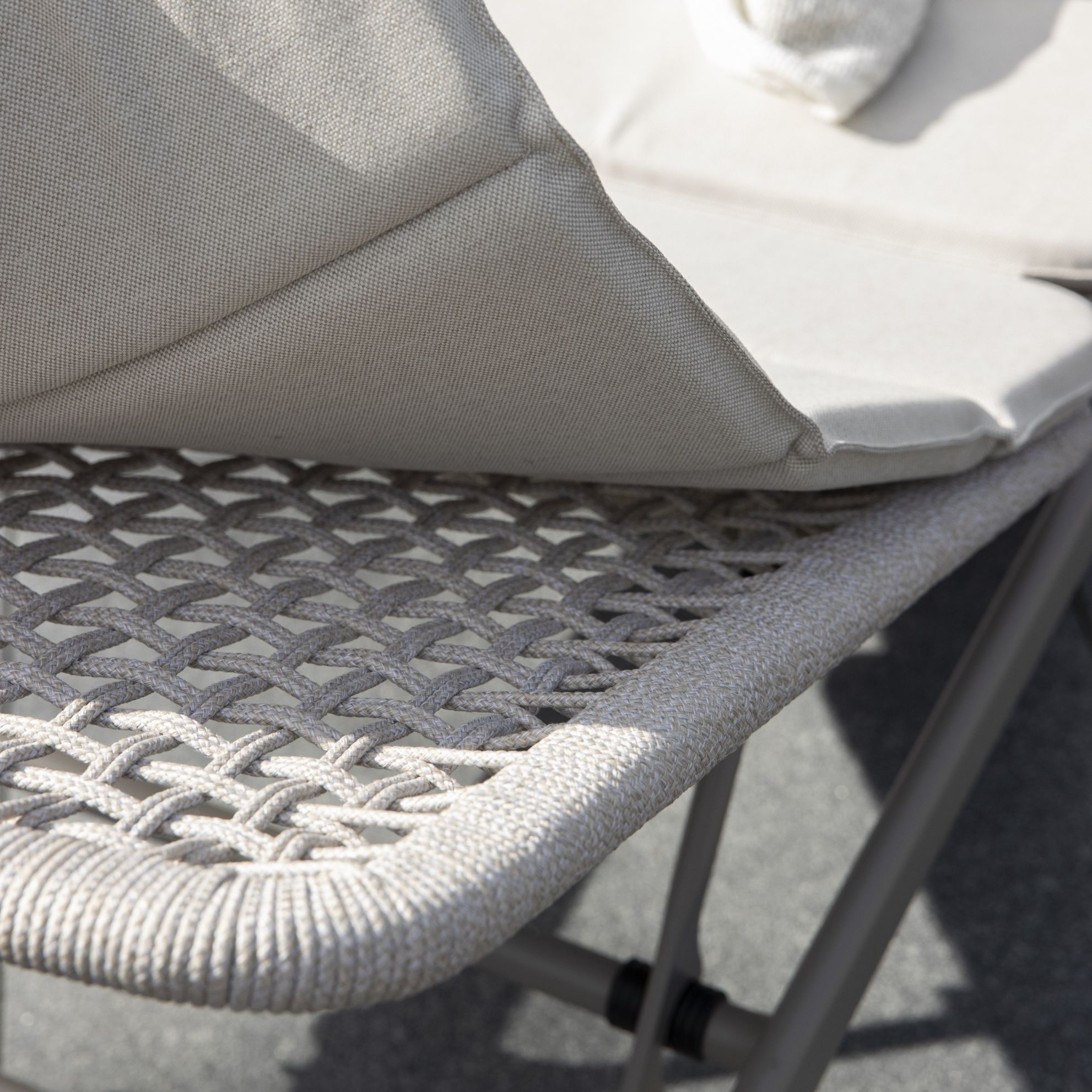 Detalj av det vävda mönstret på en solstols säte och en grå kudde.