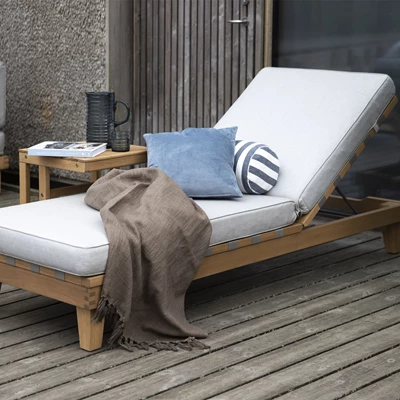 Träsolstol på en terrass med blå kudde och brunt täcke, bredvid kaffe och böcker.