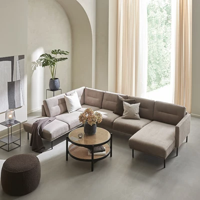 Helt vardagsrum sett ovanifrån. I rummet finns en u-soffa, ett runt soffbord med fransk rotting och svart ram, en brun puff samt några vaser och en stor tavla.