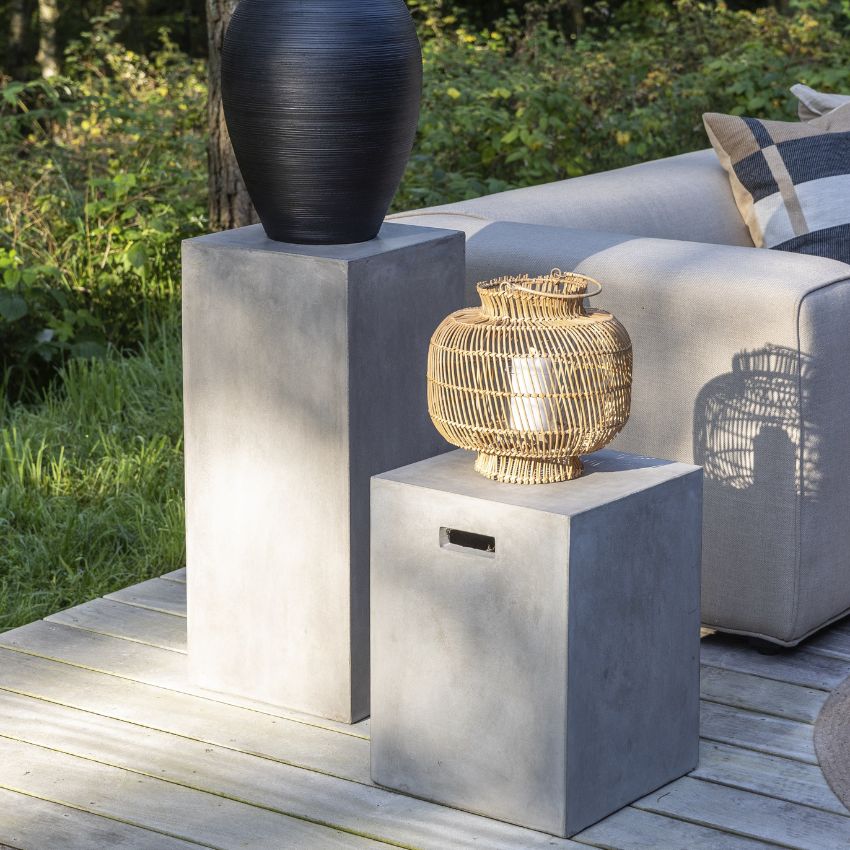 Två betongpelare med dekorativa vaser på en terrass vid moderna soffor.