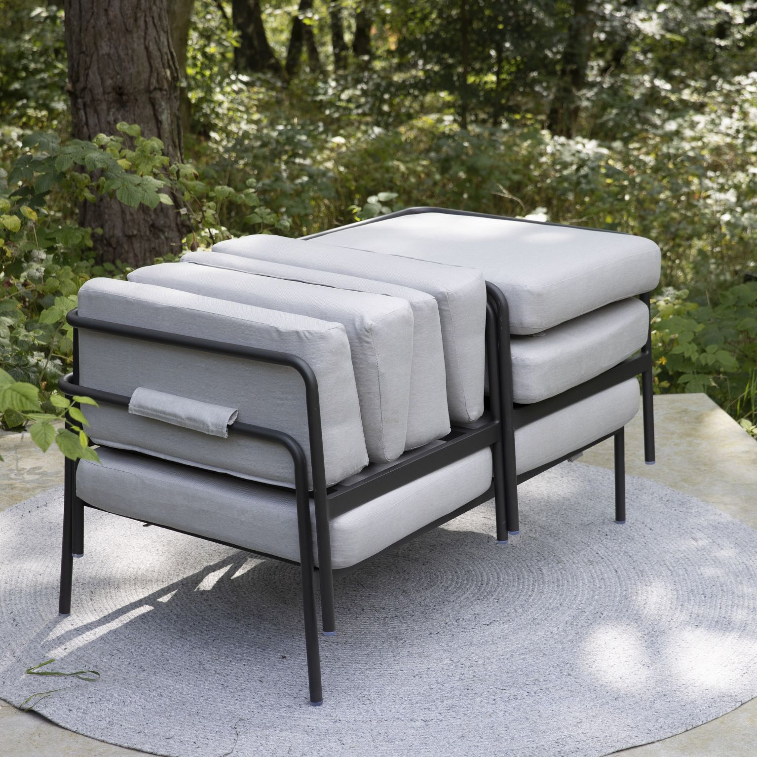 Stapel av grå kuddar på en modern utomhussoffa med svart metallram på en terrass.