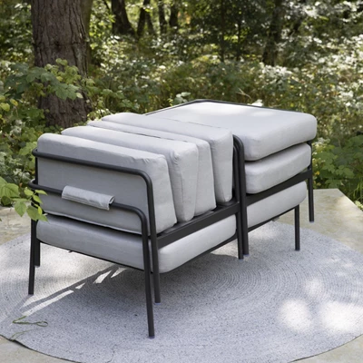 Stapel av grå kuddar på en modern utomhussoffa med svart metallram på en terrass.