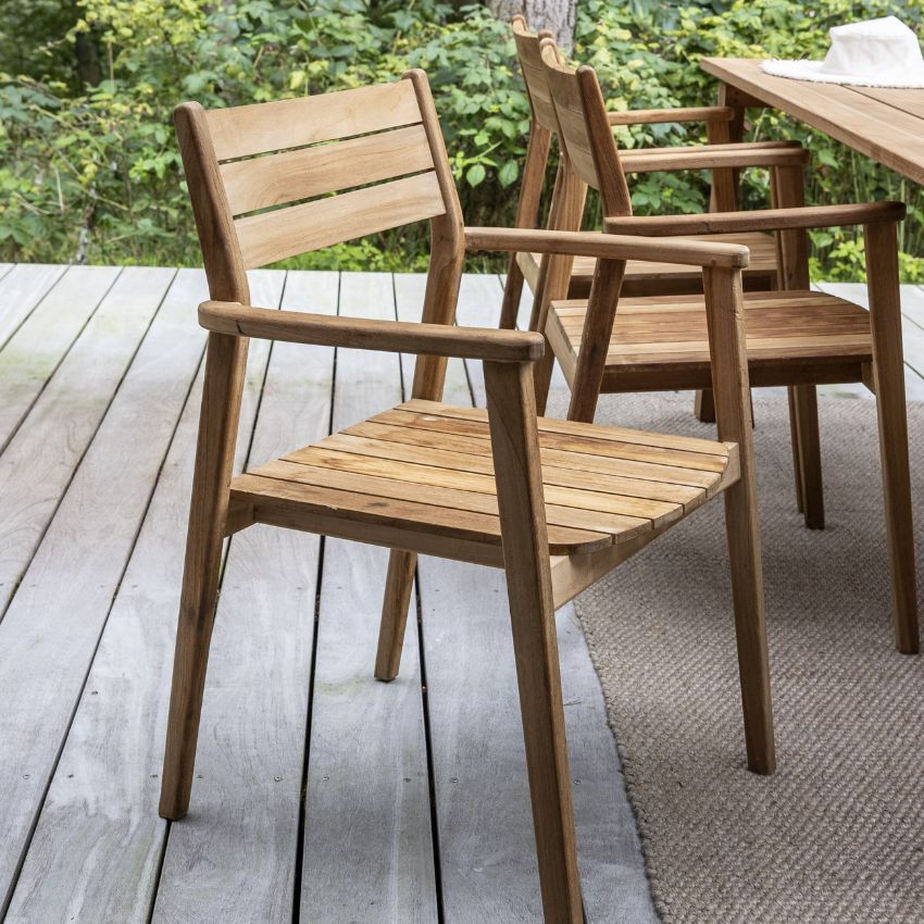 Utomhus trästolar med armstöd på en trädäck, omgivet av frodig växtlighet.