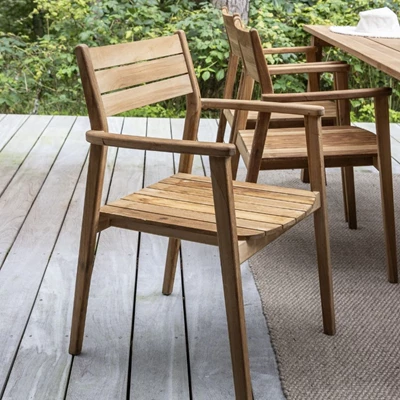 Utomhus trästolar med armstöd på en trädäck, omgivet av frodig växtlighet.