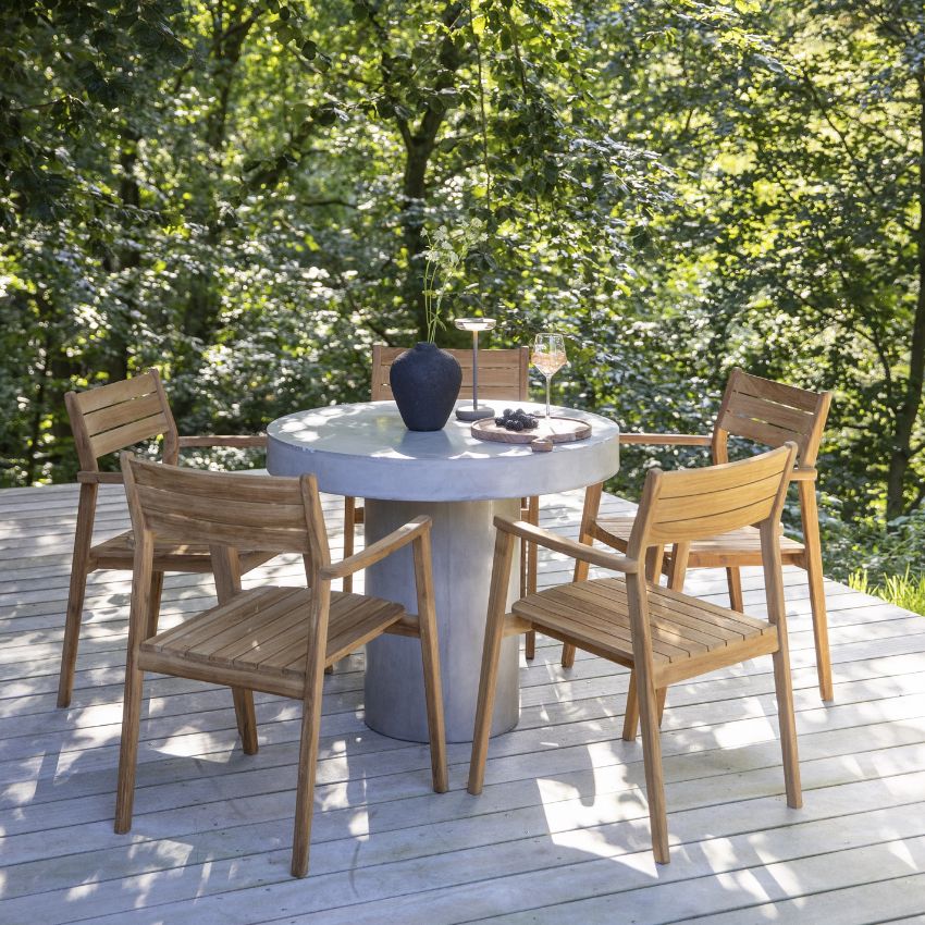 Runt utomhus matbord med trästolar, placerat på en trädterrass omgiven av träd.