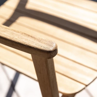 Närbild av en trästols armstöd på ett utomhus trämatbord