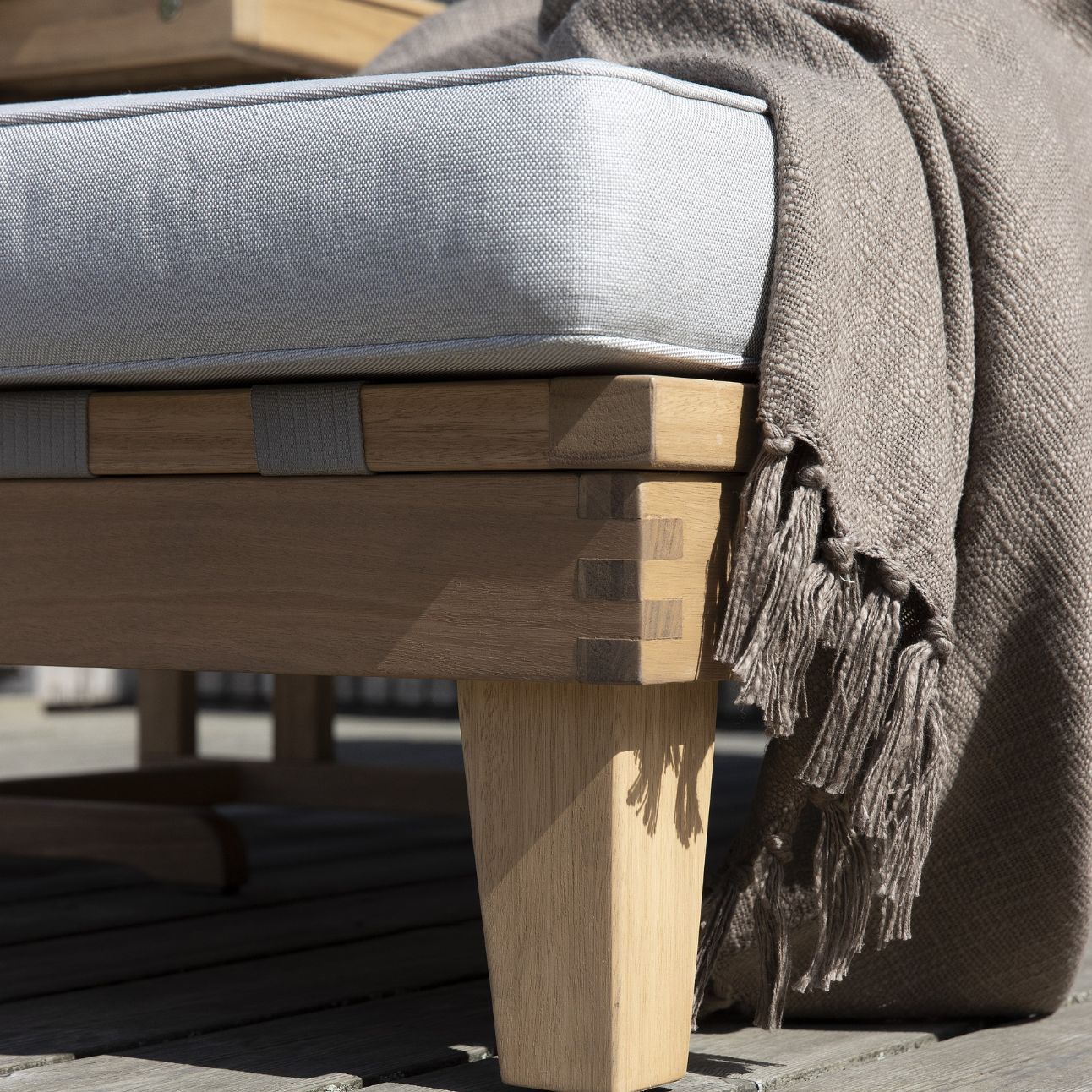 Närbild av solsäng i trä med grå kudde.