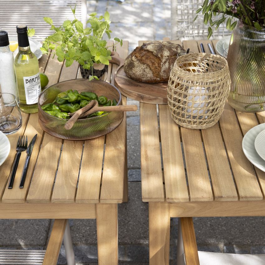 Ett utomhus träbord dukat med olika rätter, inklusive bröd och skålar med grönsaker, omgiven av naturen.