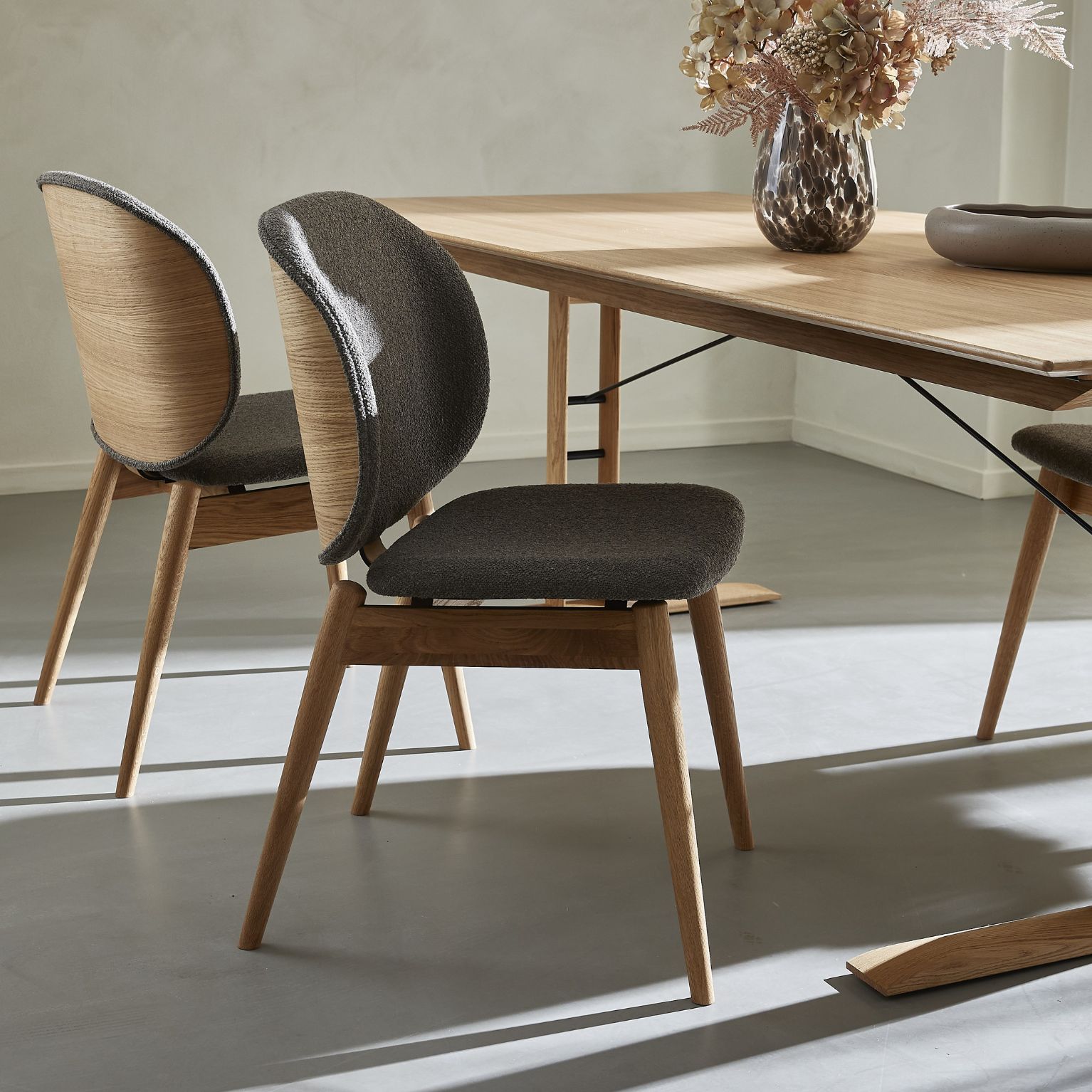 Modernt matsal med träbord och stilfulla stolar med träben och grå stoppning, i ett rum med enkel inredning.