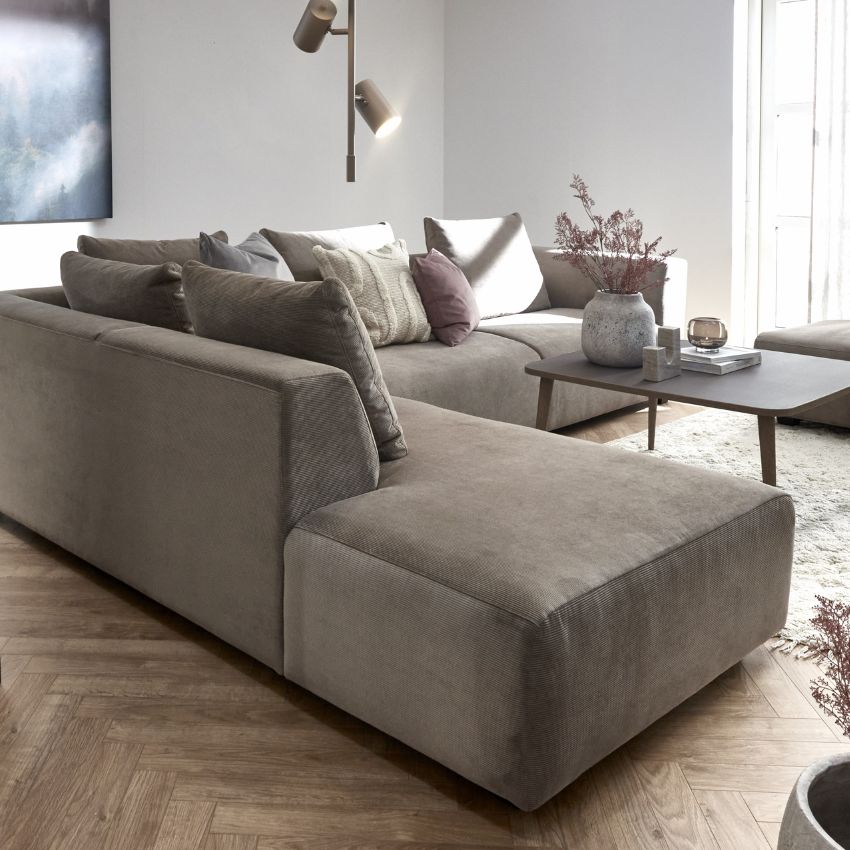 Modernt vardagsrum med en stor, brun hörnsoffa dekorerad med kuddar i neutrala färger, mörkt soffbord och dekorativa detaljer