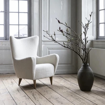 Elegant vit loungestol med träben i ett rum med klassiska fönster och en minimalistisk look.