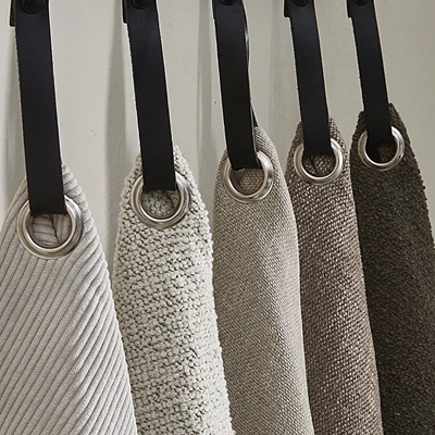 Fem tygprover i olika beige och bruna nyanser, upphängda med svarta läderremmar och metallringar