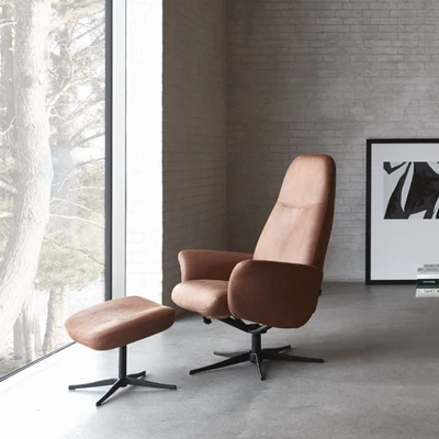 Bekväm brun fåtölj med matchande fotpall placerad i ett minimalistiskt rum med stora fönster och betongväggar