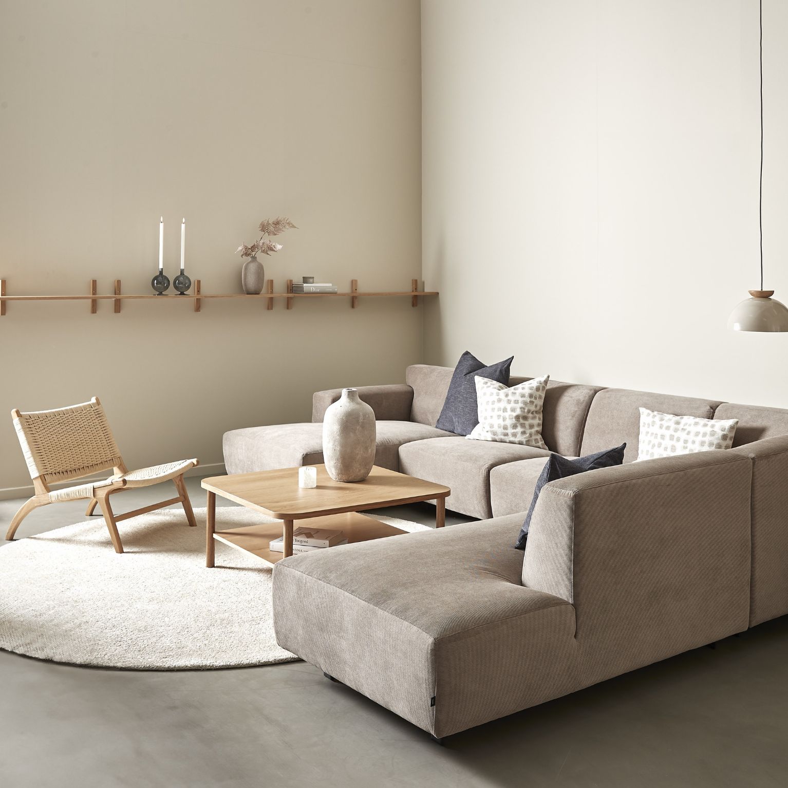 Modern beige hörnsoffa kombinerad med en trästol, en rund matta och en minimalistisk väggdesign för en harmonisk atmosfär