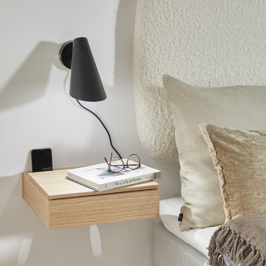 Vägglampa i svart som hänger över sängbord.