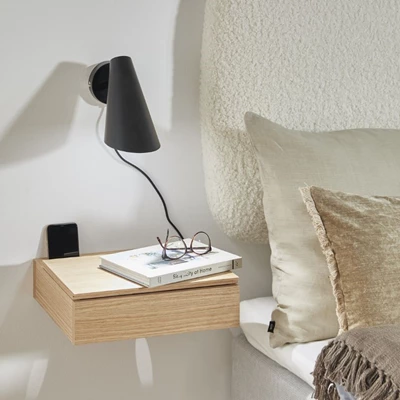 Vägglampa i svart som hänger över sängbord.