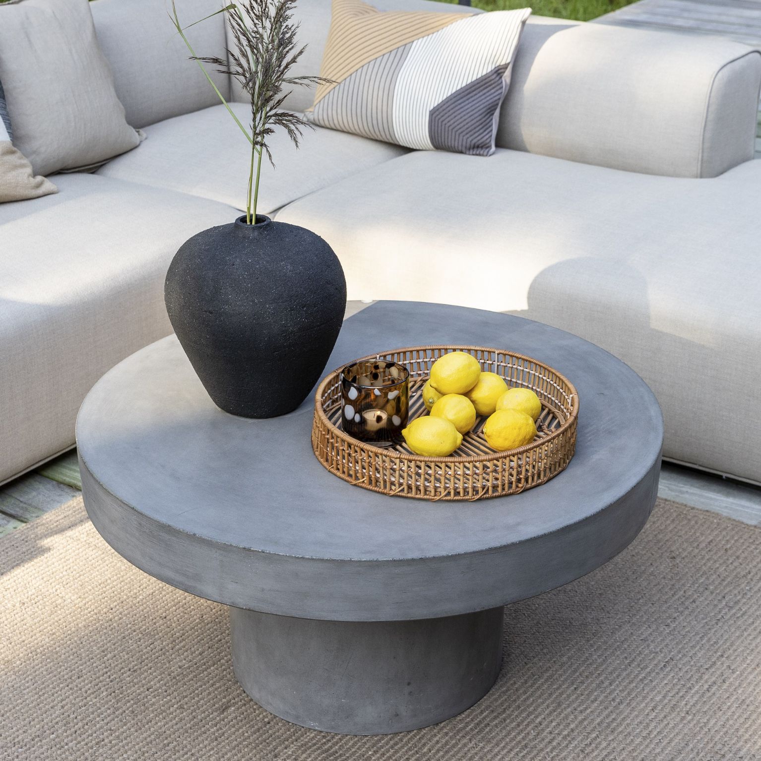 Runt och robust lounge trädgårdsbord i fibercement med loungesoffa i bakgrunden.