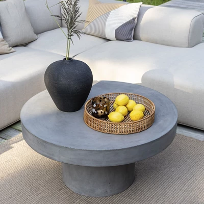 Runt och robust lounge trädgårdsbord i fibercement med loungesoffa i bakgrunden.