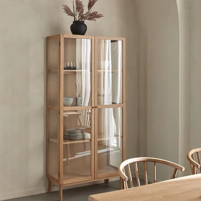 Hög vitrinskåp i trä med glasdörrar och dekoration ovanpå.