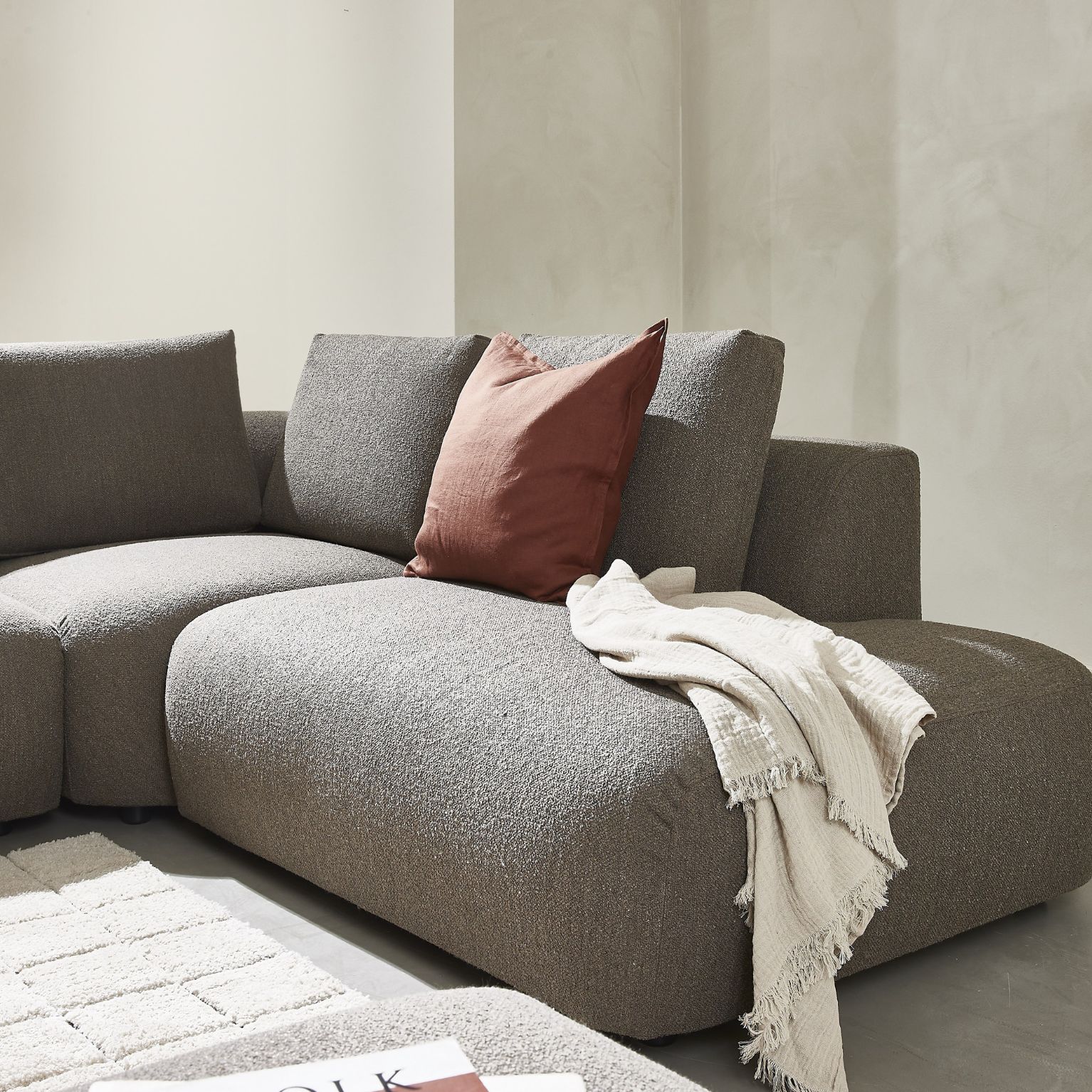 Antracitgrå modulsoffa med röd prydnadskudde och vitt täcke ovanpå