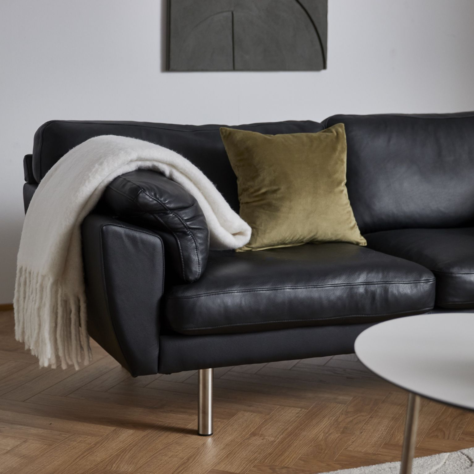 Sort lædersofa med gullig pyntepude og hvidt tæppe hængende på armlæn