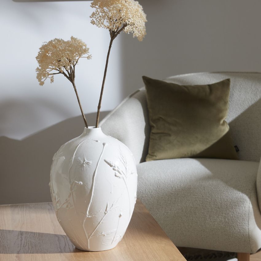 Vit vas med strukturmönster på bord med vita blommor.