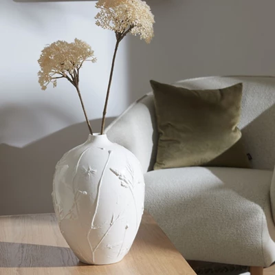 Vit vas med strukturmönster på bord med vita blommor.