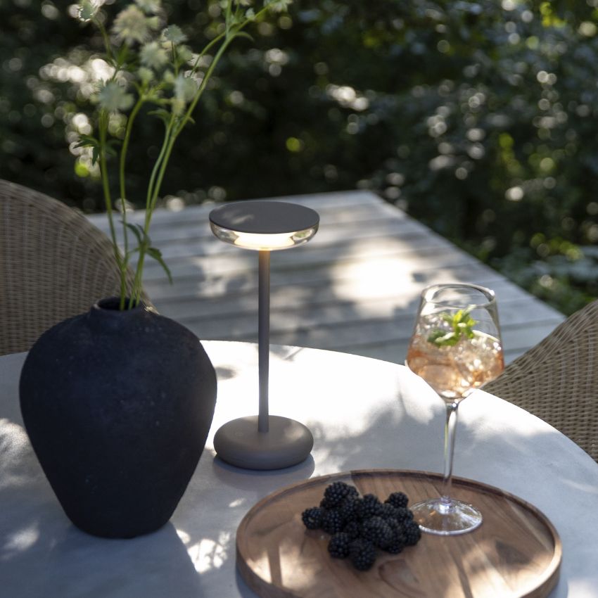 Utebord med trådlös bordslampa, svart vas samt en bricka med ett glas vin och några blåbär.