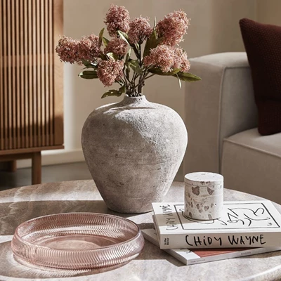 Grå kruka på bord tillsammans med ljusrosa fat och liten förvaringsburk i marmor.