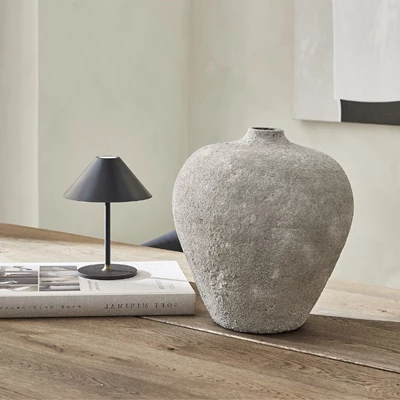 Grå kruka stående på bord med liten svart lampa bredvid.