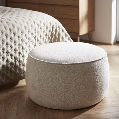 Rund puff i vitt stående på golvet framför sängen