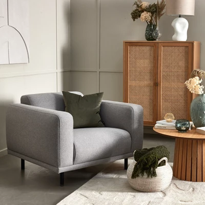 Fåtölj med svarta ben stående vid vit matta, litet sidobord samt ett vitrinskåp i rotting bakom