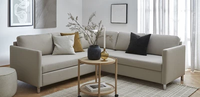 Hörnsoffa i grå design stående i vardagsrumsmiljö med soffbord, matta och tavlor hängande på väggen