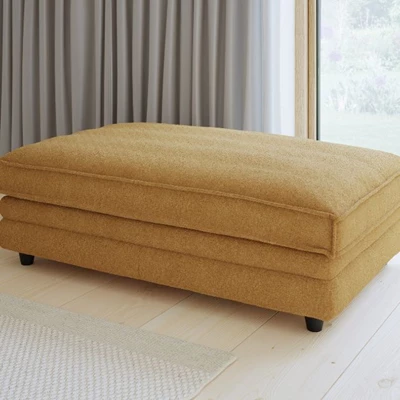 Gul puff stående på golvet med gardiner hängande bakom